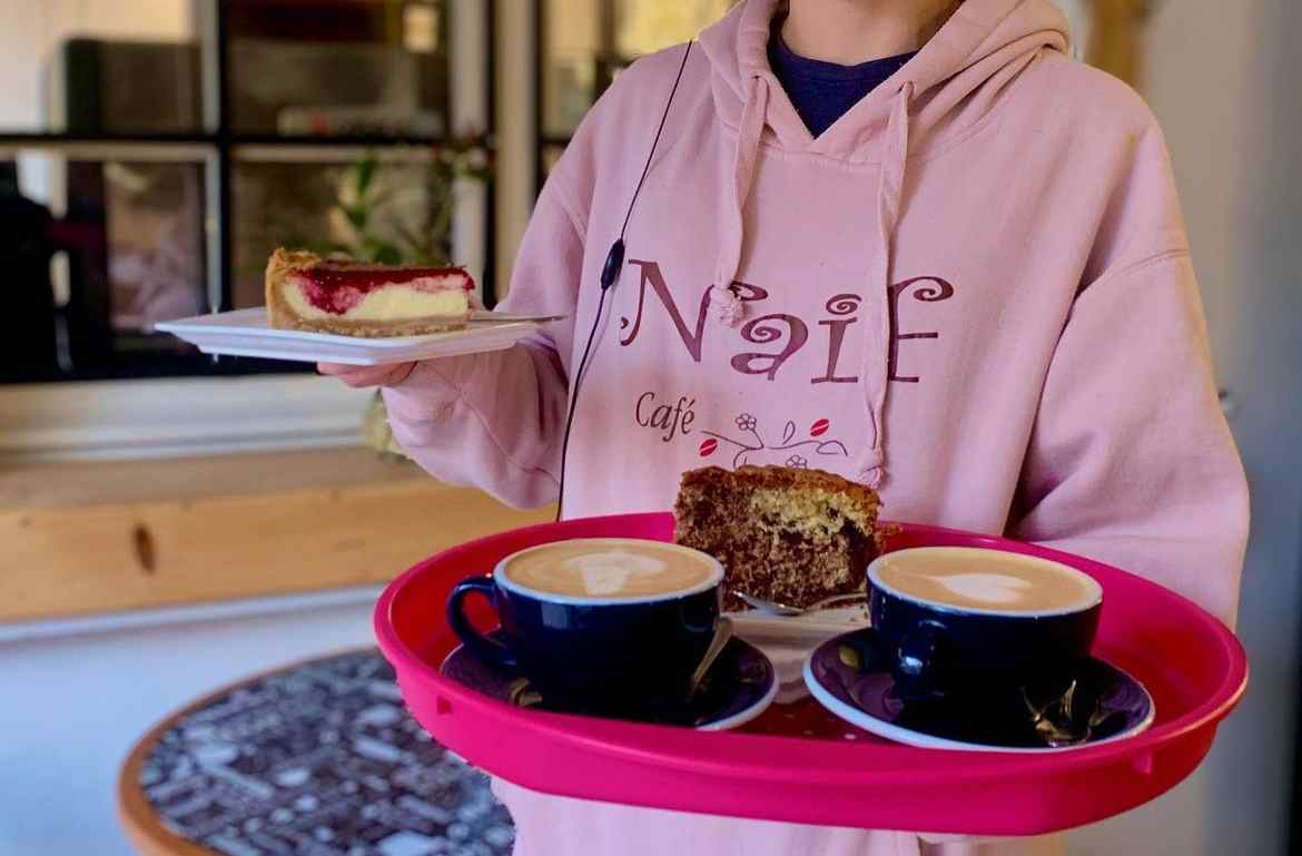 Mujer sosteniendo bandeja con cafés y pasteles. Del Instagram @naifcafe_cl