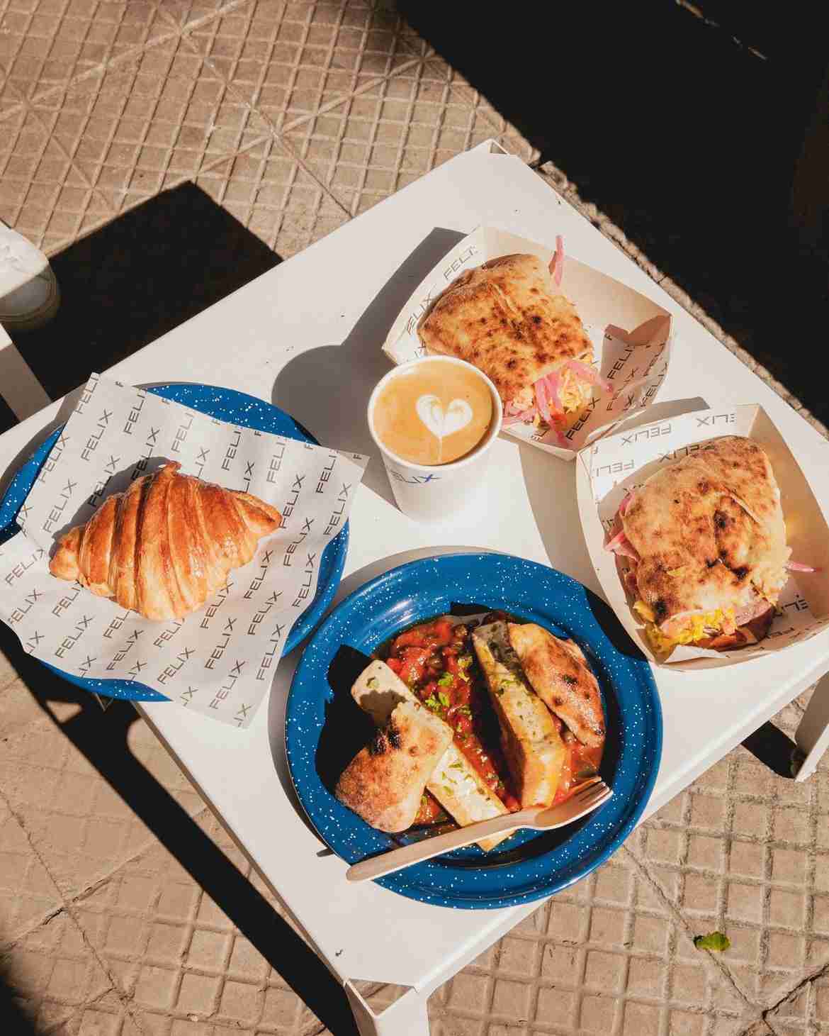 Cuatro platos de comida al rededor de un café, apoyados en una mesa. Del Instagram @felixcafe.cl