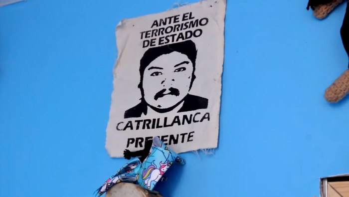 Fotografía de la pared de la pieza de Millaray Jara, en el medio tiene colgado un poster con la ilustración del rostro de Camilo Catrillanca y el texto: "Ante el terrorismo de Estado Catrillanca presente". Justo abajo del poster hay un pañuelo celeste con estampado de unicornios.

Foto por Antonia Montoya. 
